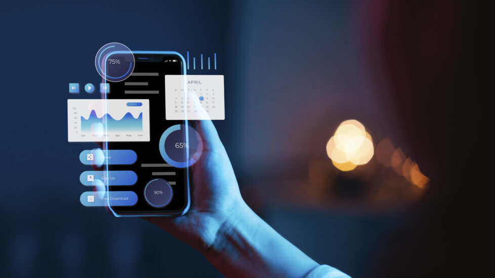 Person holding a smartphone with futuristic digital interface showing data charts, calendar, and progress bars, representing modern mobile app development technology.